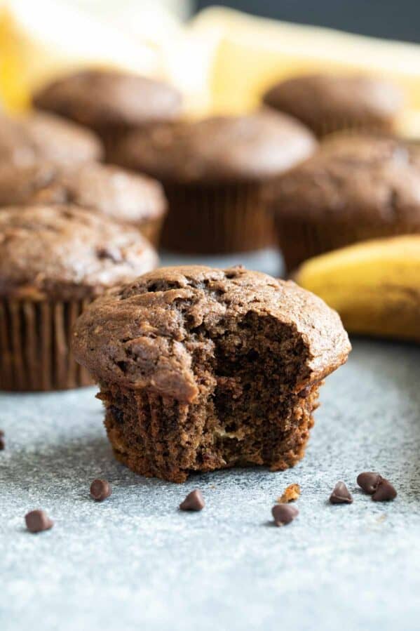 Chocolate Banana Muffin with a bite taken from it with mini chocolate chips around the muffin.