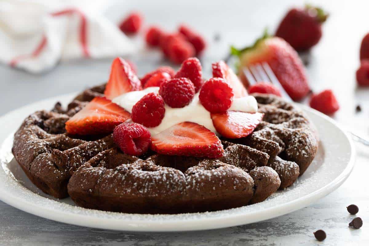 Chocolate waffle on a plate topped with whipped cream and fresh berries.