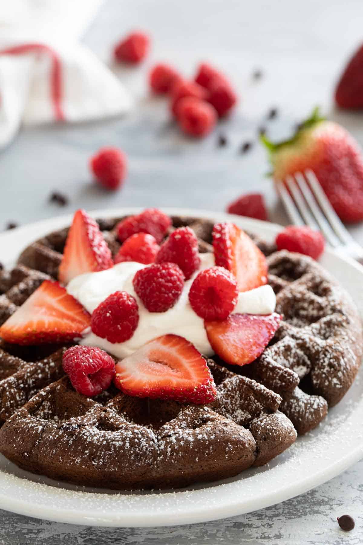 Chocolate Waffle topped with berries and whipped cream with berries in the background.