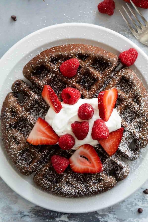 Chocolate waffle topped with powdered sugar, whipped cream, and berries.