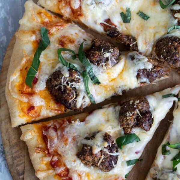Meatball pizza cut into slices, topped with fresh basil.