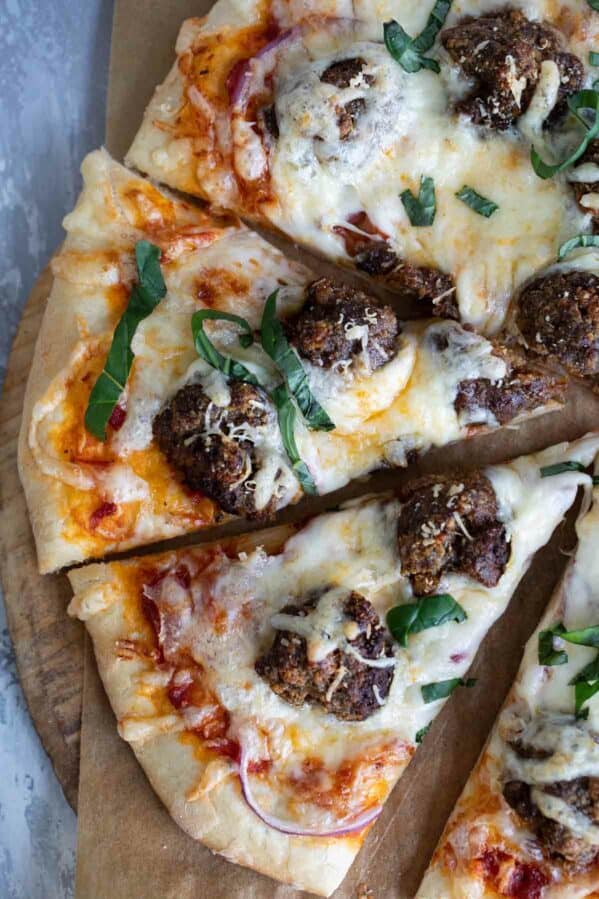 Meatball pizza cut into slices, topped with fresh basil.