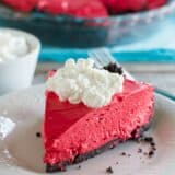 Slice of no bake red velvet cheesecake with the rest of the cheesecake in the background.