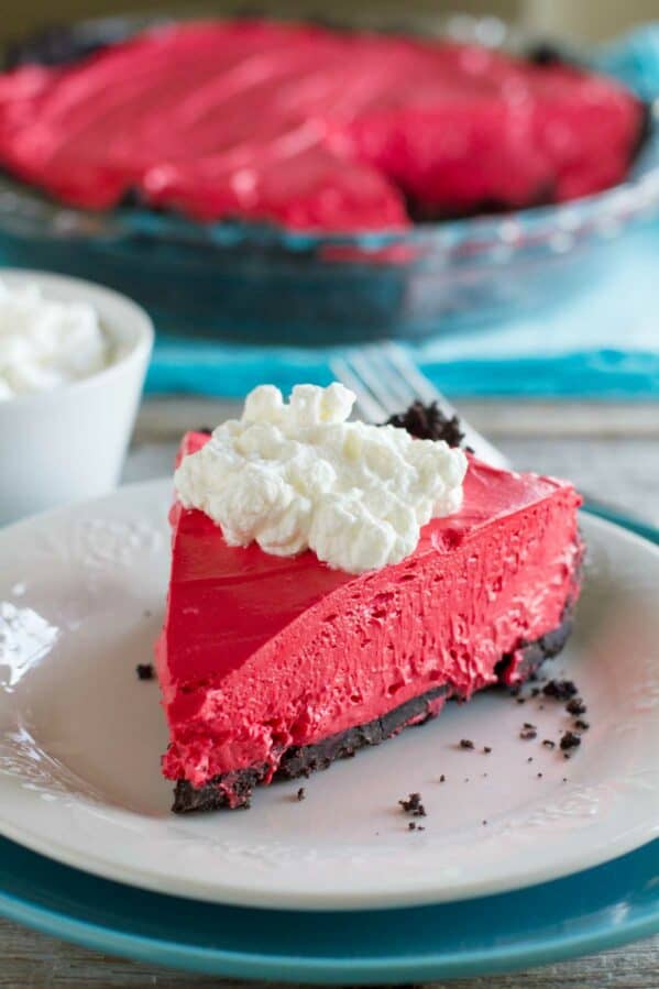 Slice of no bake red velvet cheesecake with the rest of the cheesecake in the background.