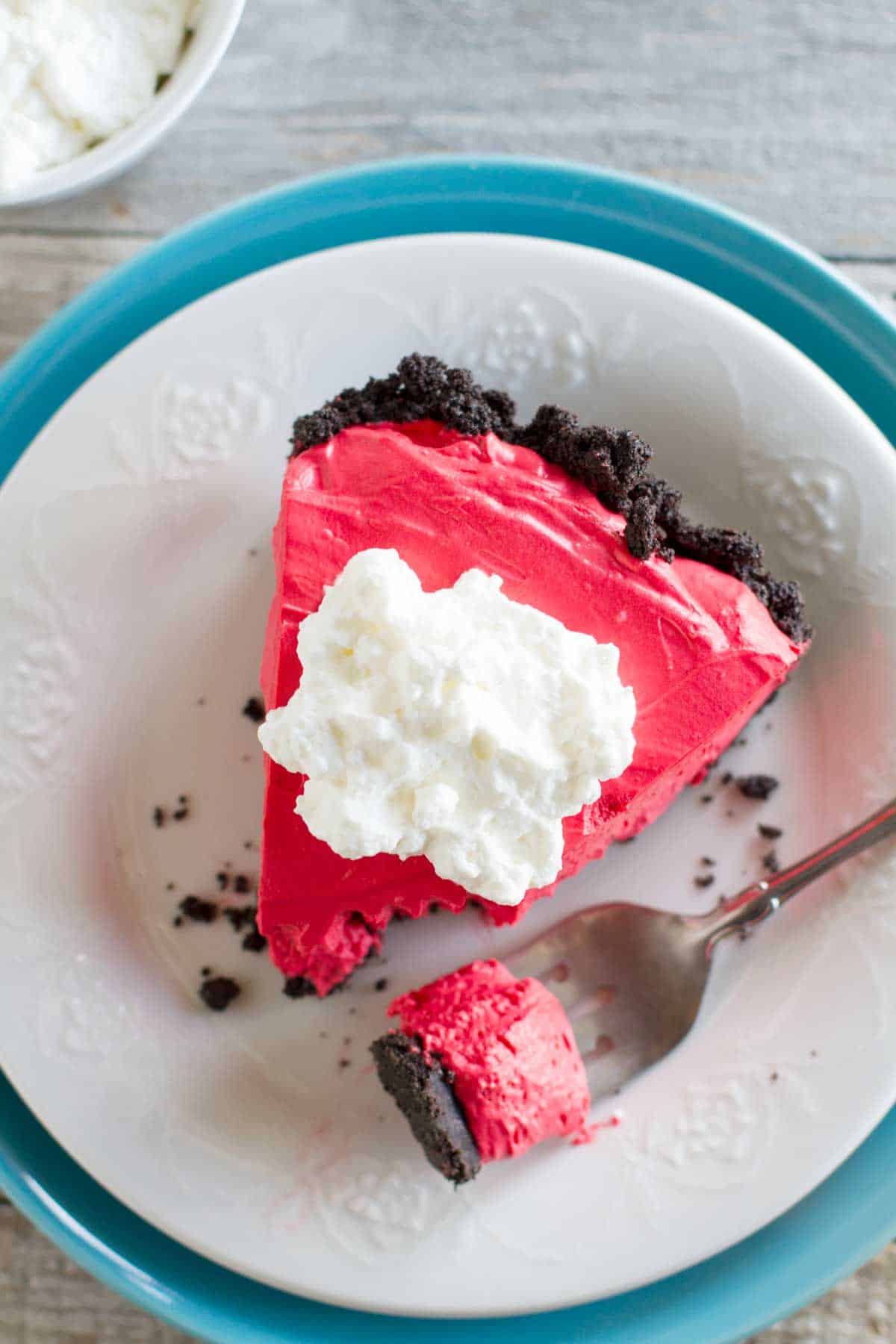 Slice of no bake red velvet cheesecake topped with whipped cream.
