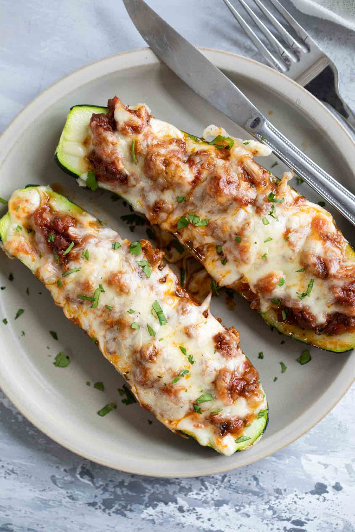 Two stuffed zucchini boat halves on a plate with a knife next to them.