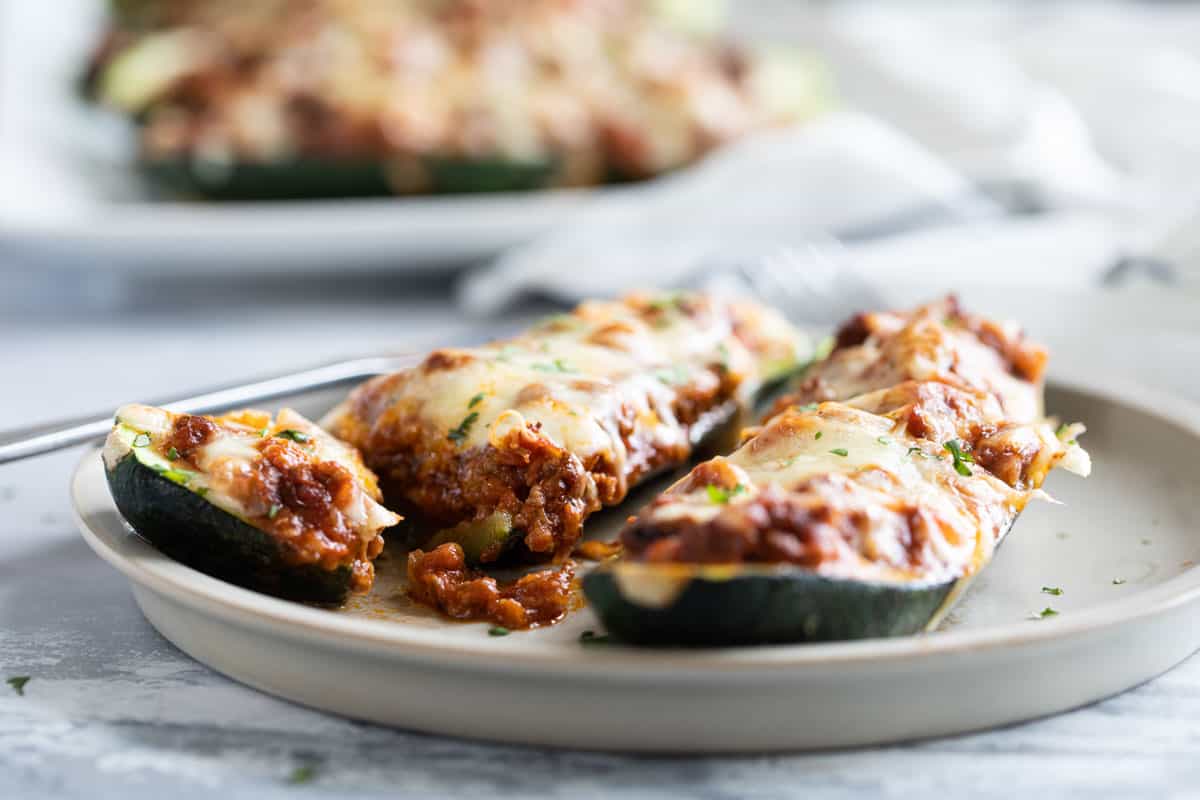 Stuffed zucchini boats on a plate with one cut in half.