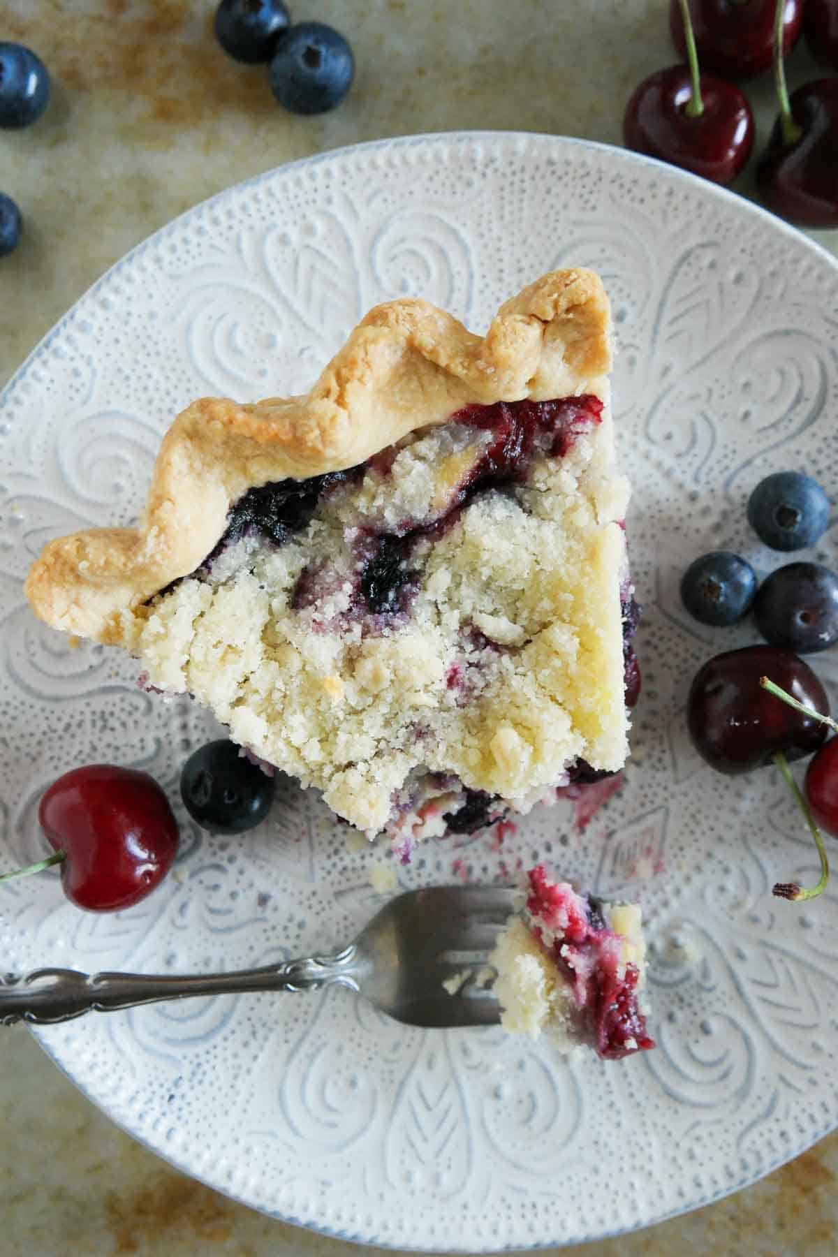 Slice of cherry and blueberry cream pie with a fork full of pie taken from it.