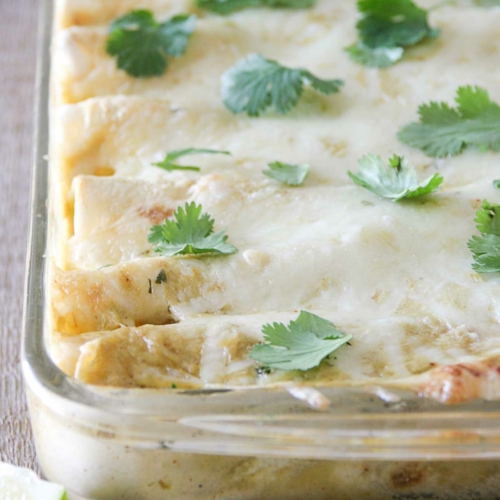 Pan filled with chicken, black bean, and zucchini enchiladas topped with green chile sauce and cheese.