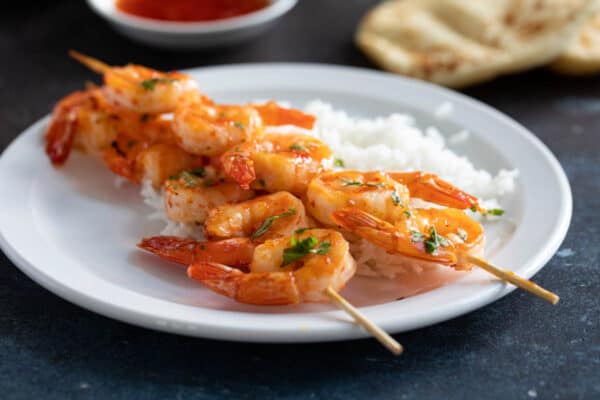 Two chili honey garlic shrimp kabobs on a plate served with rice.