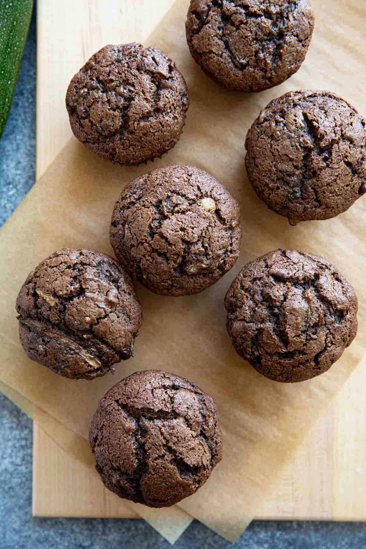 Chocolate zucchini muffins on parchment paper on top of a wooden board.