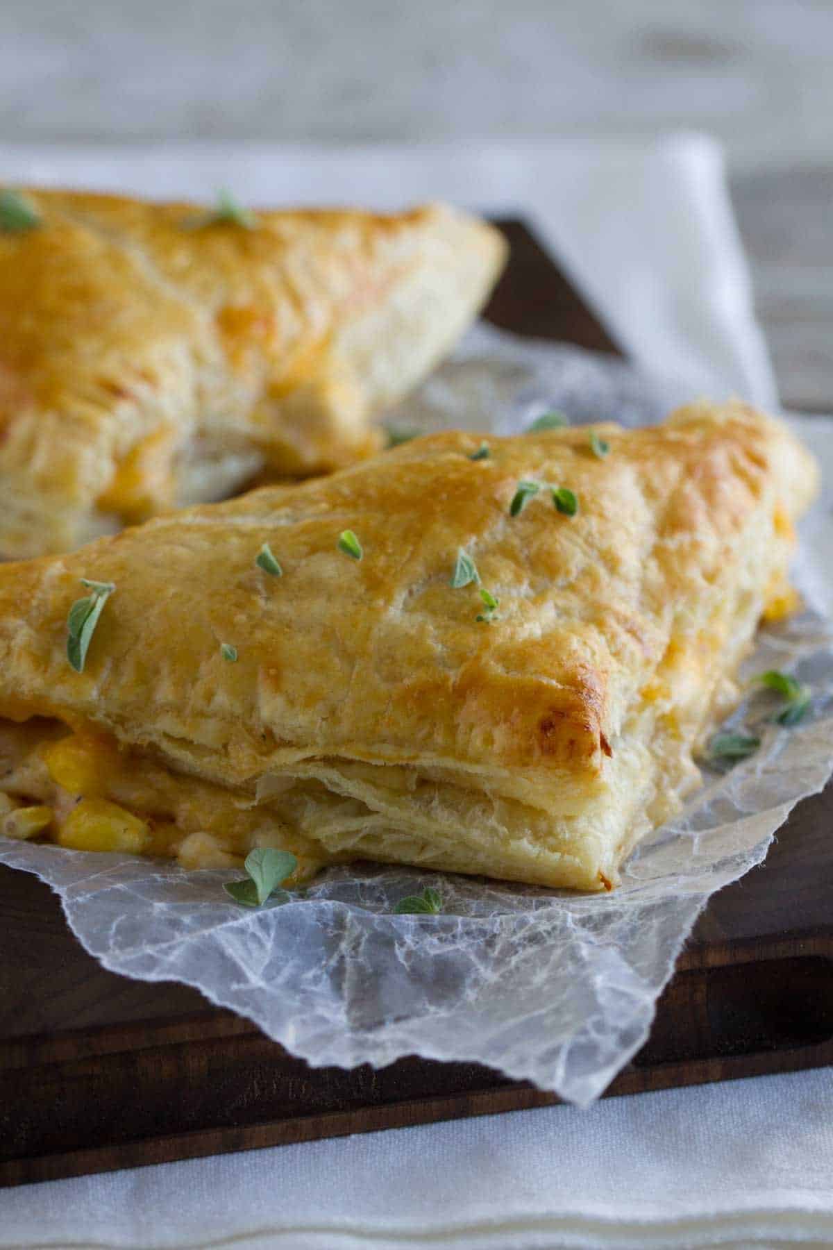 Two creamy chicken and corn turnovers on a cutting board sprinkled with thyme.