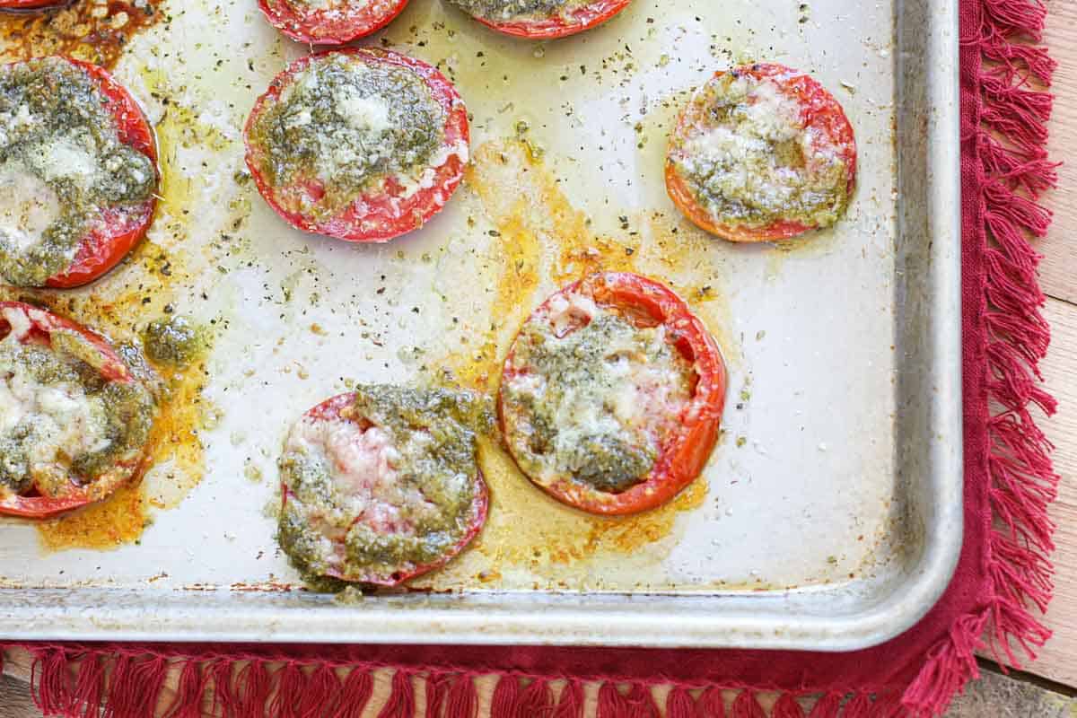 Baking pan with roasted tomatoes topped with parmesan cheese and pesto.