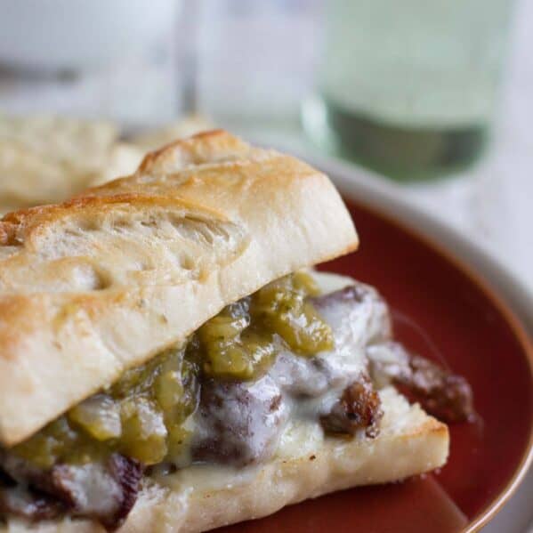 Sandwich topped with steak, melted cheese, and salsa verde.