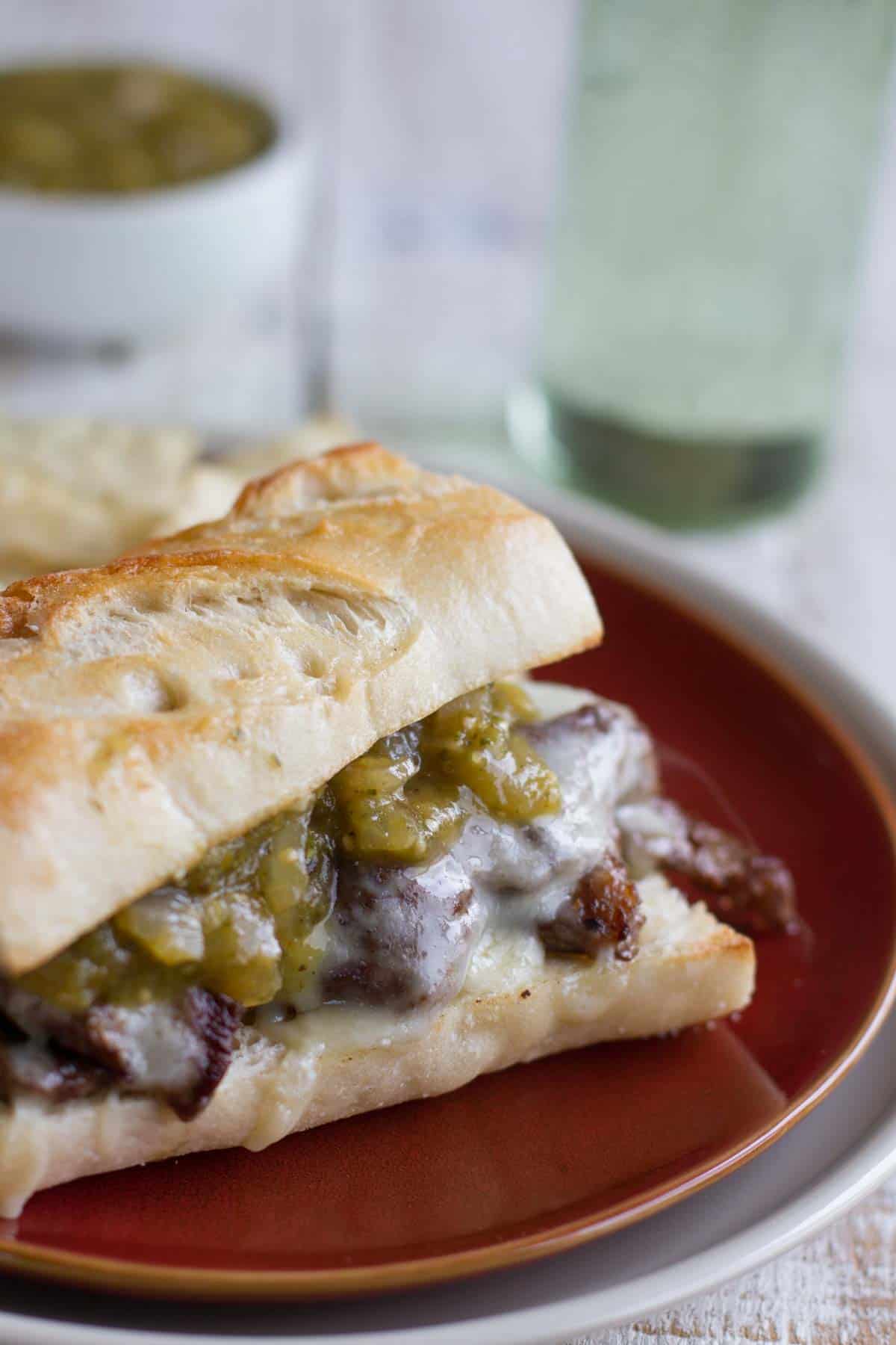 Sandwich topped with steak, melted cheese, and salsa verde.
