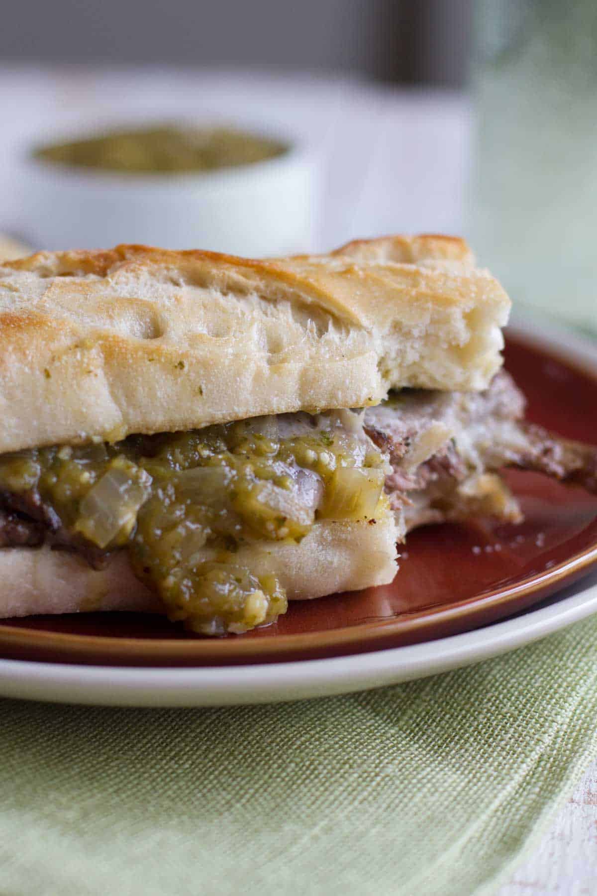 Salsa verde steak sandwiches on a plate with salsa verde dripping off.