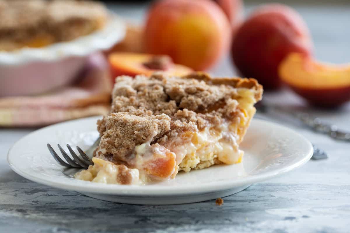 Slice of Sour Cream Peach Pie on a plate with a fork.