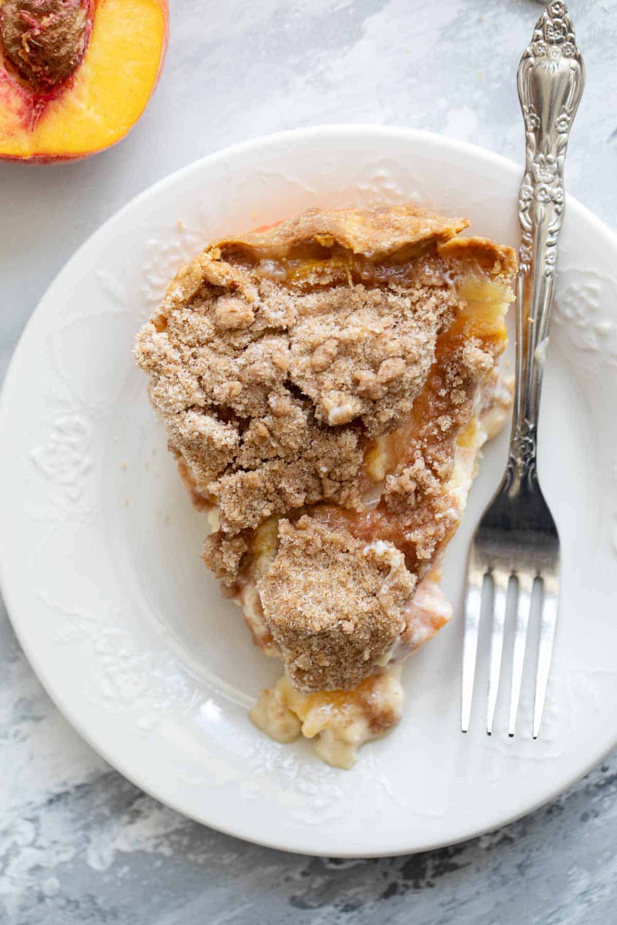 Slice of sour cream peach pie on a plate with a fork.