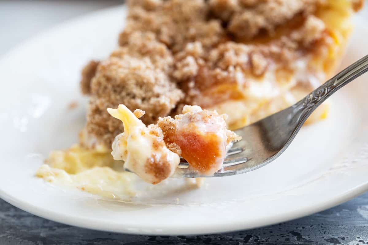 Bite of sour cream peach pie on a fork with the rest of the slice behind it.