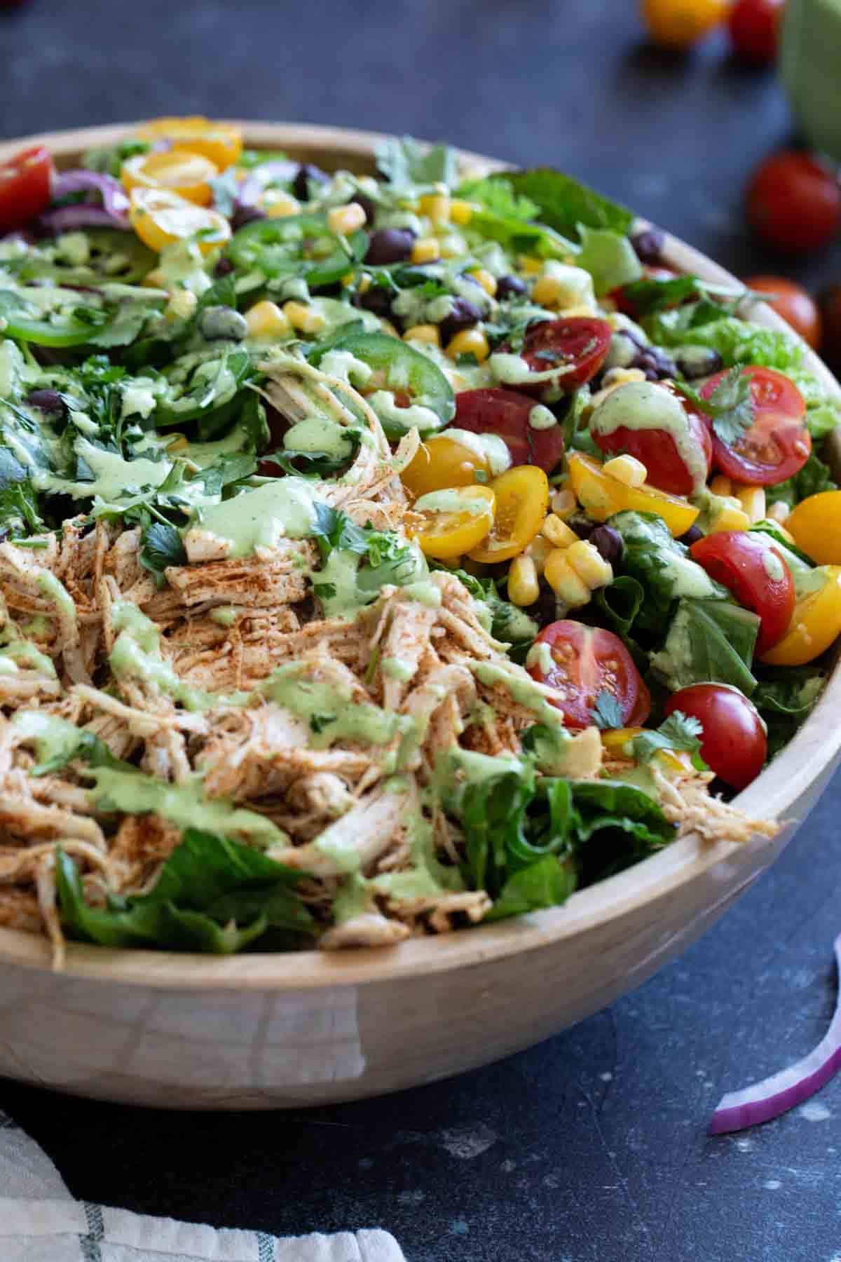 Southwest chicken salad in a wooden bowl, topped with spicy cilantro dressing.