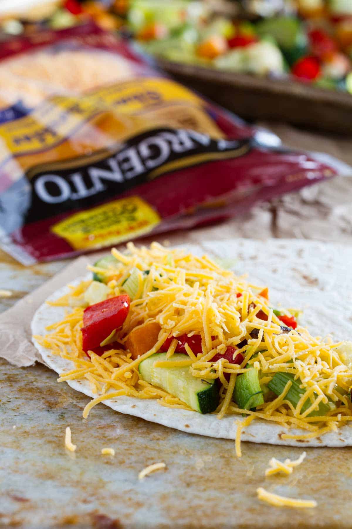 Filling a tortilla with cheese and roasted vegetables.