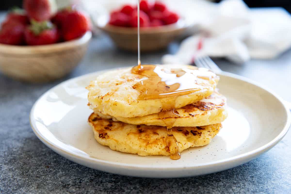 Three cottage cheese pancakes with syrup being poured on top.