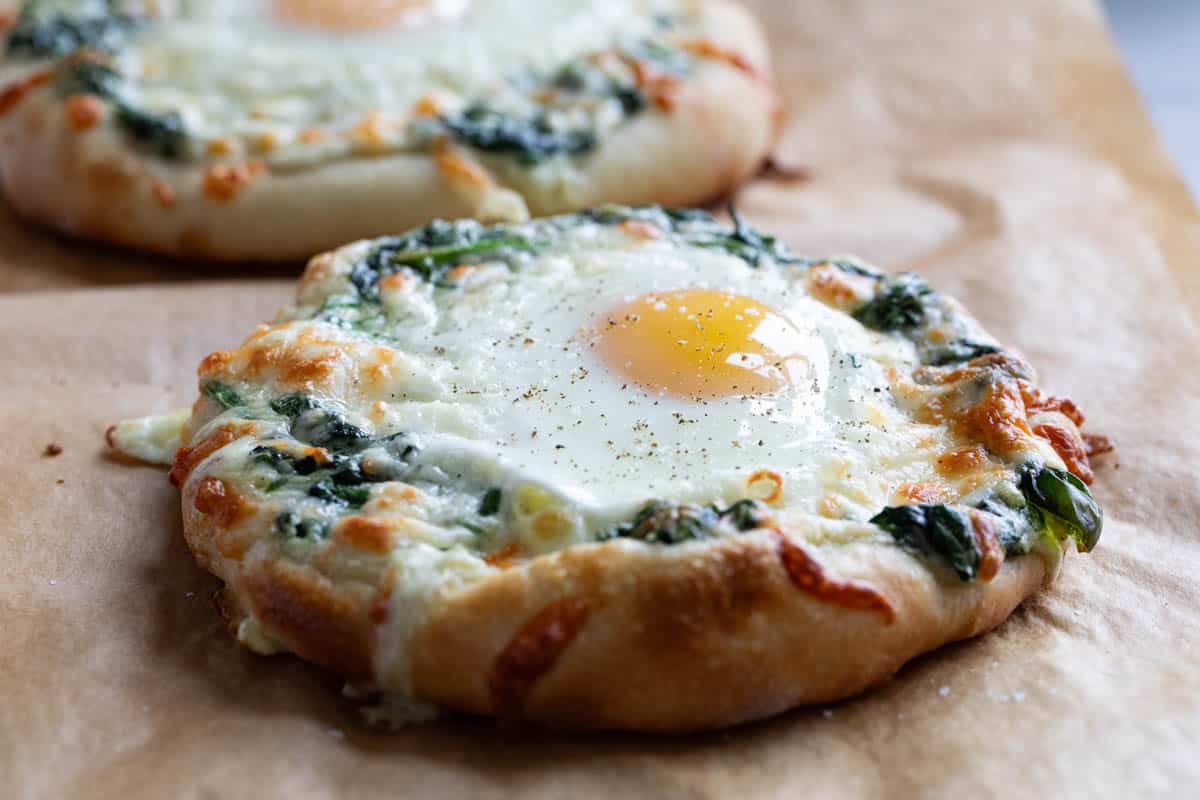 Individual Egg Pizza topped with creamed spinach and a sunny side up egg.