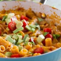 One pan enchilada pasta in a blue skillet, topped with tomatoes and avocado.