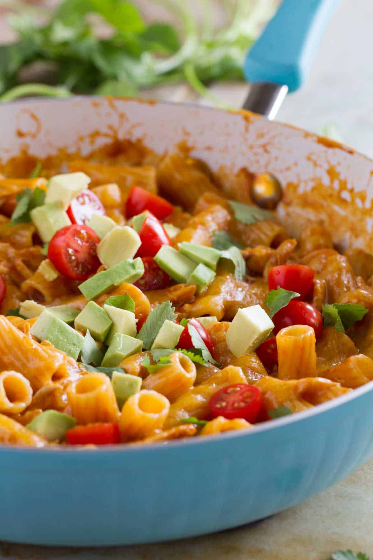 One pan enchilada pasta in a blue skillet, topped with tomatoes and avocado.