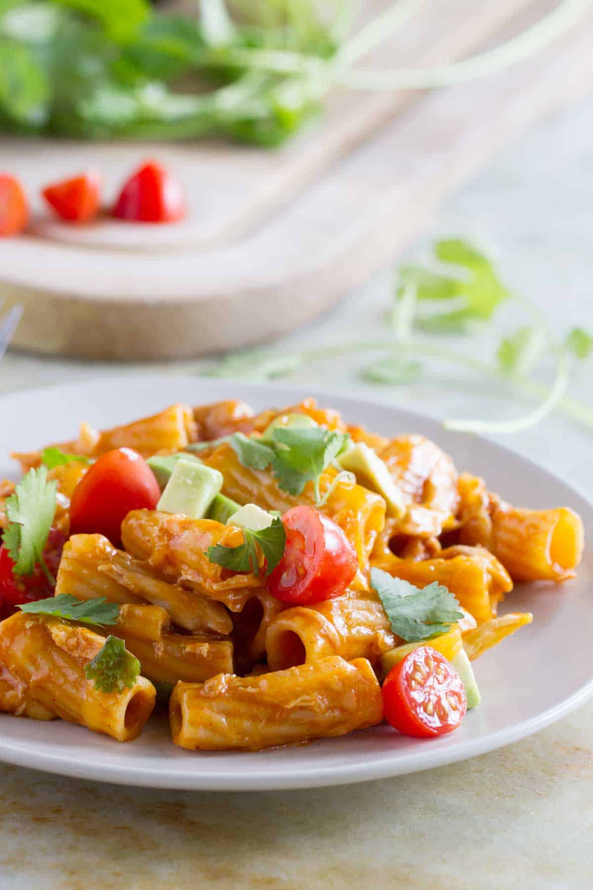 Enchilada pasta on a plate, topped avocado, tomatoes, and cilantro.