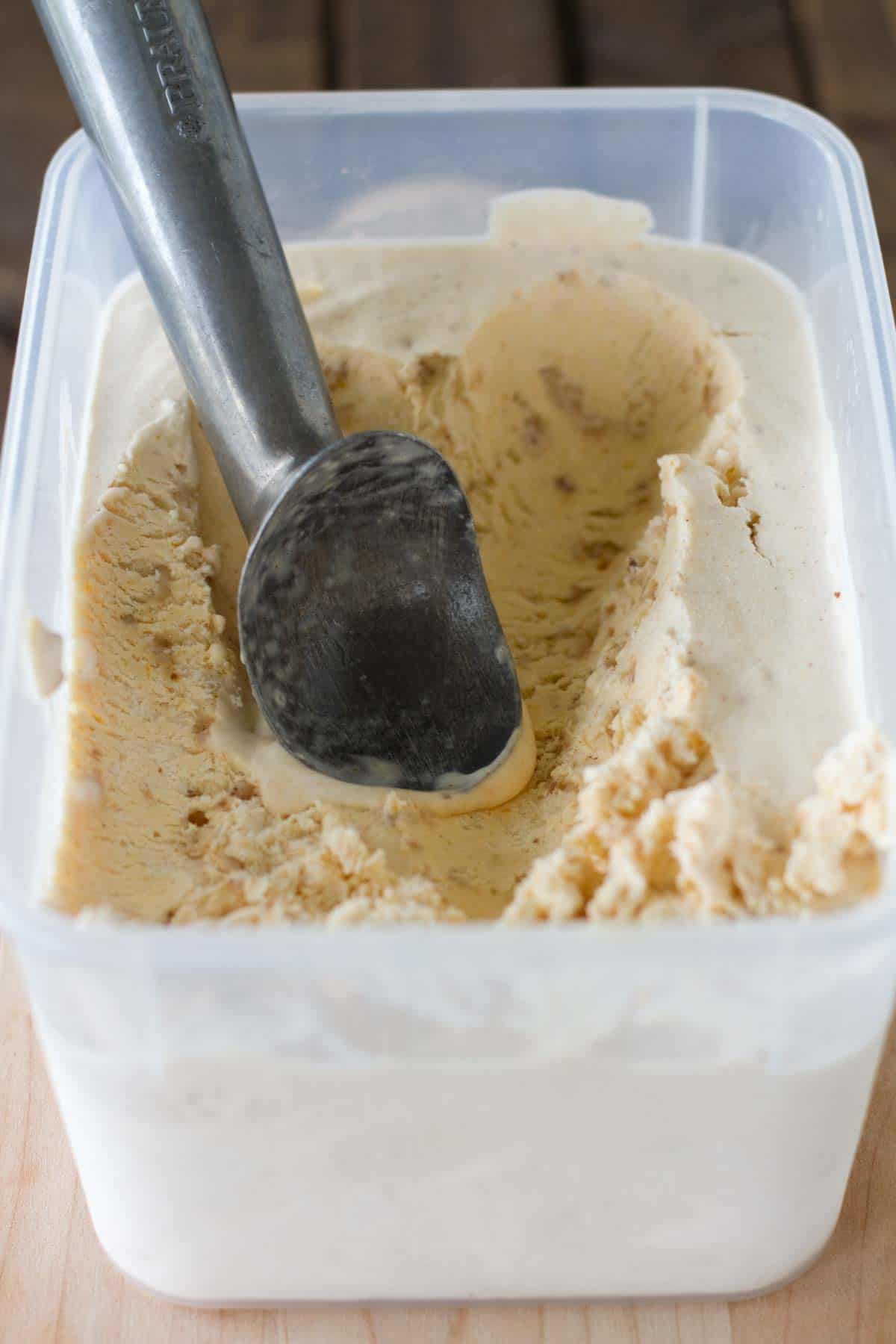 Pumpkin ice cream in a container with an ice cream scoop.