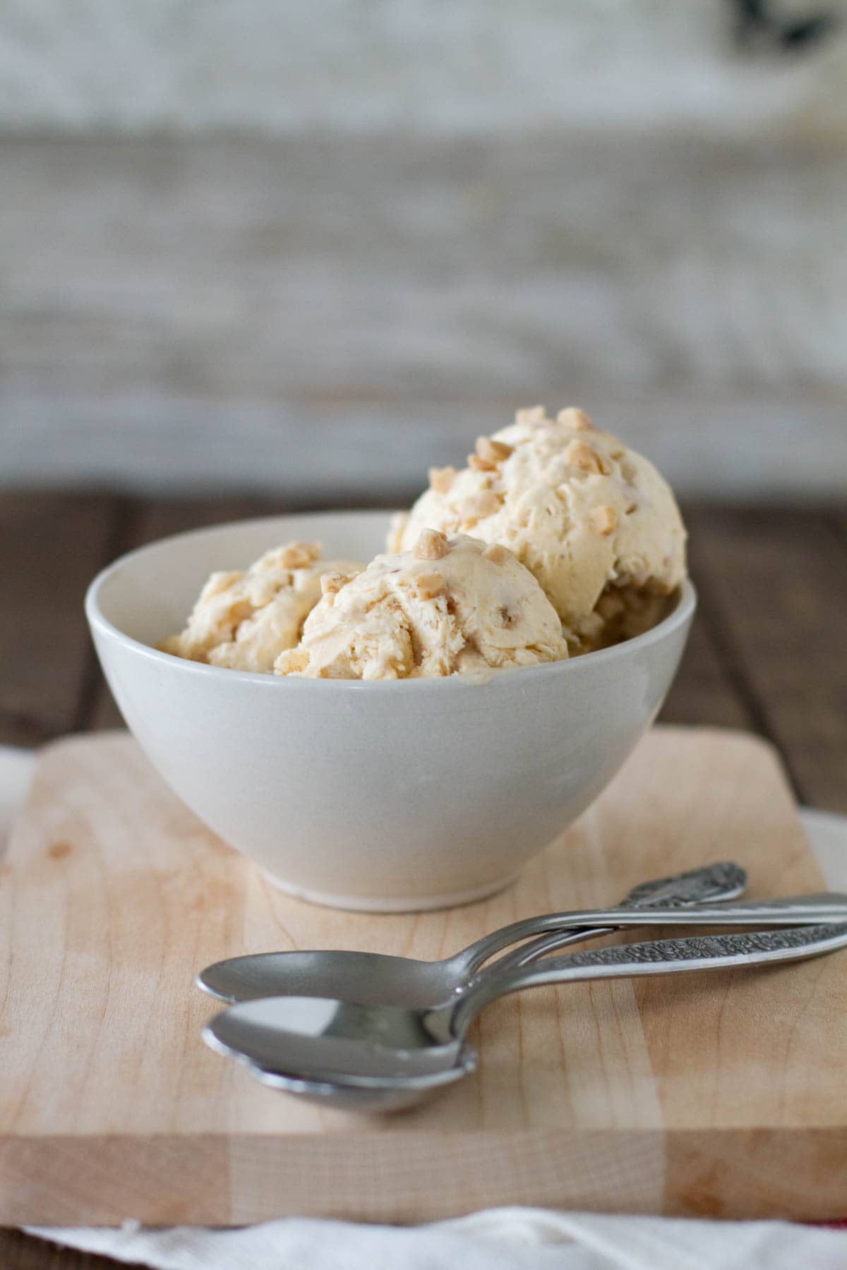 Bowl filled with pumpkin ice cream with toffee with spoons in front.