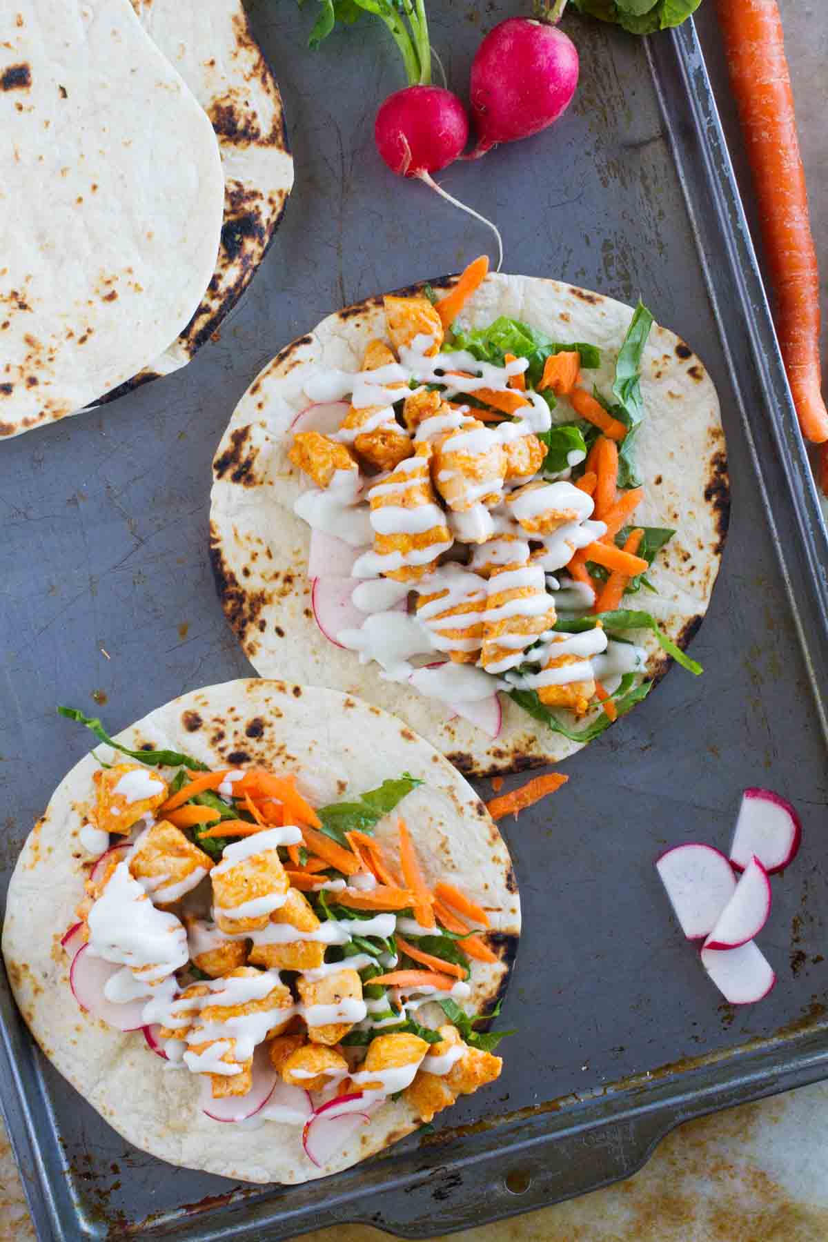 Buffalo chicken tacos open on a baking sheet.