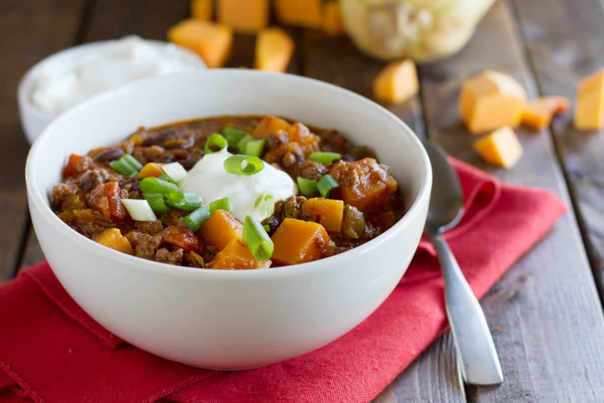 Bowl of butternut squash chili with beef on a red cloth.