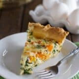 Slice of butternut squash quiche with kale with a fork on a plate.