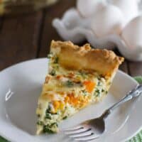 Slice of butternut squash quiche with kale with a fork on a plate.