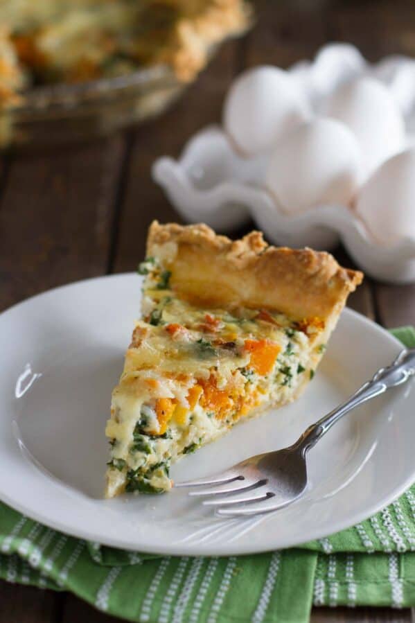 Slice of butternut squash quiche with kale with a fork on a plate.