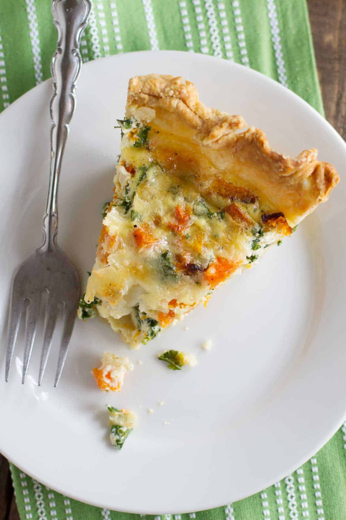 Slice of butternut squash quiche with kale on a plate with a bite taken from it.