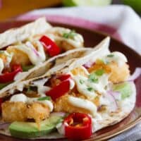 Two crispy shrimp tacos topped with homemade mayonnaise on a plate.