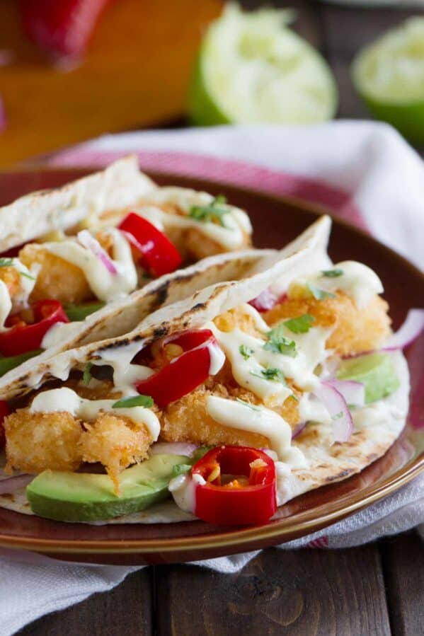Two crispy shrimp tacos topped with homemade mayonnaise on a plate.