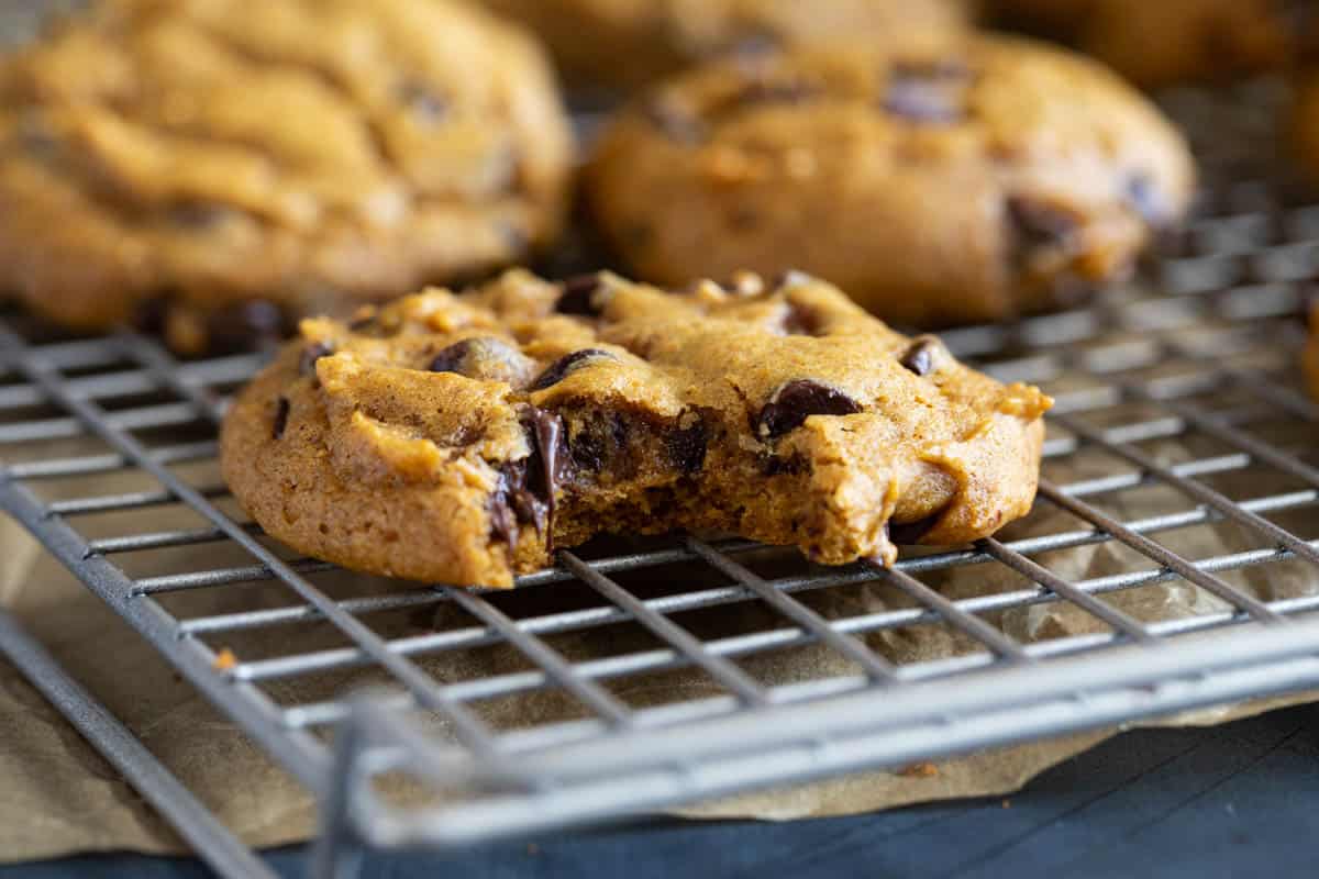 Pumpkin chocolate chip cookie with a bite taken from it on a cooling rack.