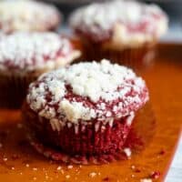 Red velvet muffins on a wooden board with the wrapper peeled away from one muffin.