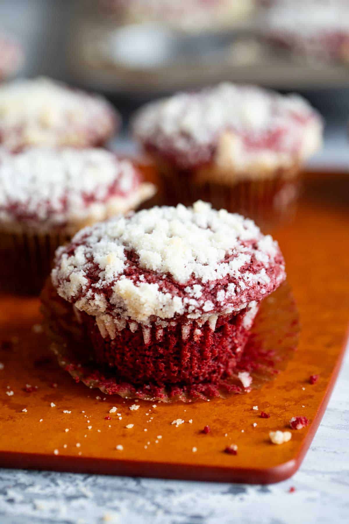 Red velvet muffins on a wooden board with the wrapper peeled away from one muffin.