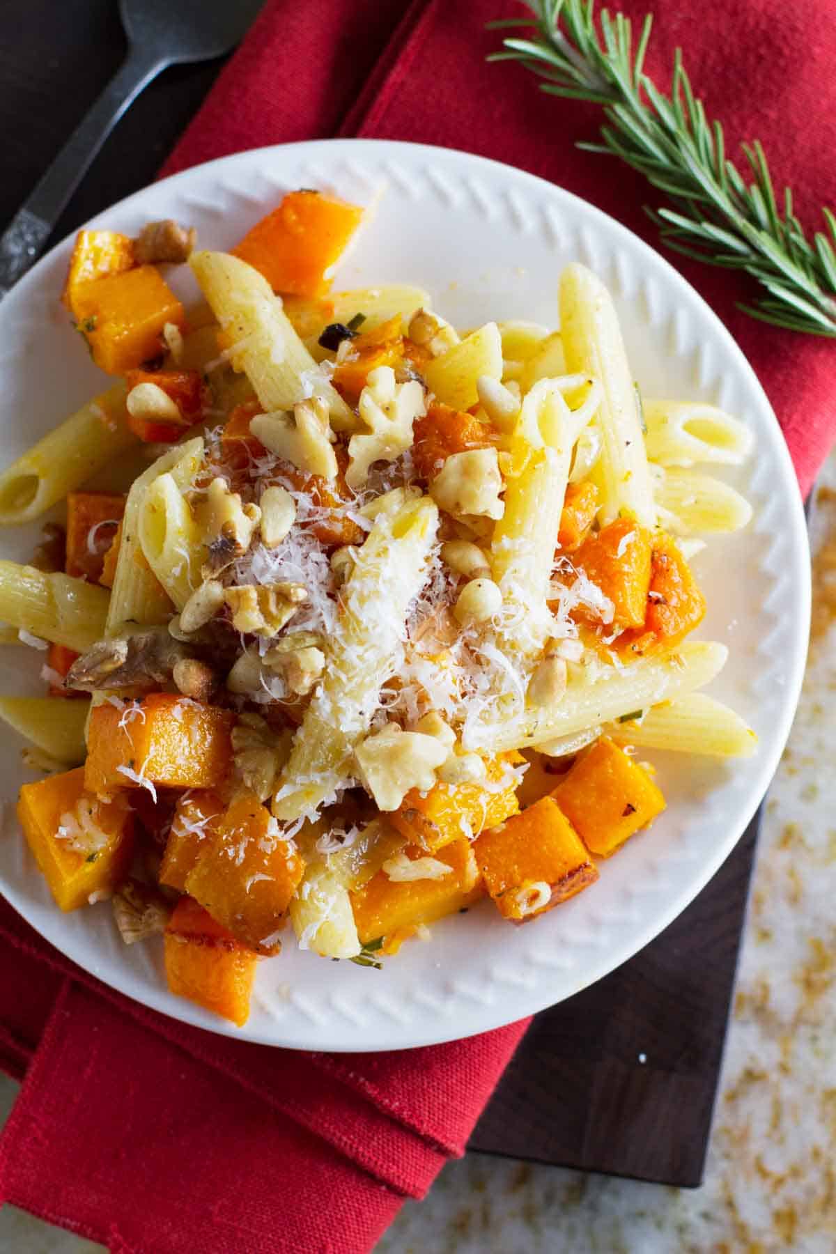 Plate filled with penne pasta, roasted butternut squash, walnuts, and rosemary.
