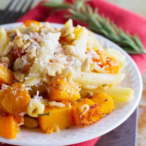 Plate filled with roasted butternut squash cubes and pasta, topped with parmesan cheese.