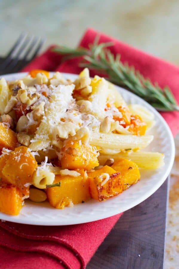 Plate filled with roasted butternut squash cubes and pasta, topped with parmesan cheese.