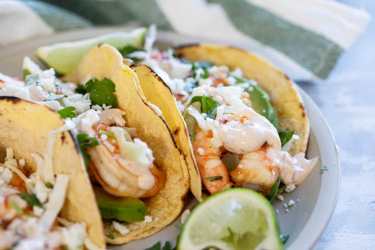 Plate with shrimp tacos topped with queso fresco, cabbage, and homemade chipotle lime crema.