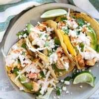 Three shrimp tacos on a plate, topped with cabbage, cheese, and chipotle lime crema.