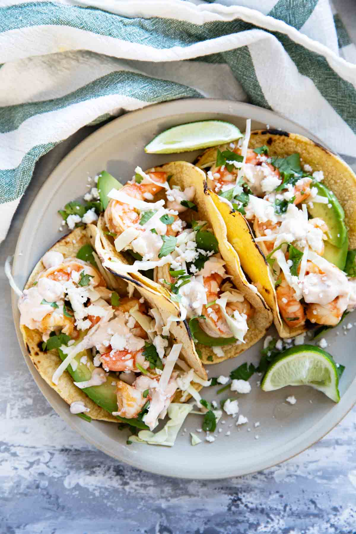 Three shrimp tacos on a plate, topped with cabbage, cheese, and chipotle lime crema.