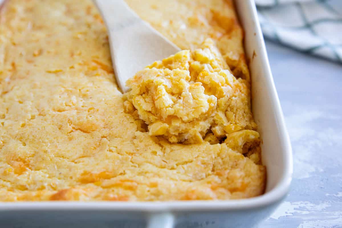 Casserole dish of corn casserole with a wooden spoon dishing some out.